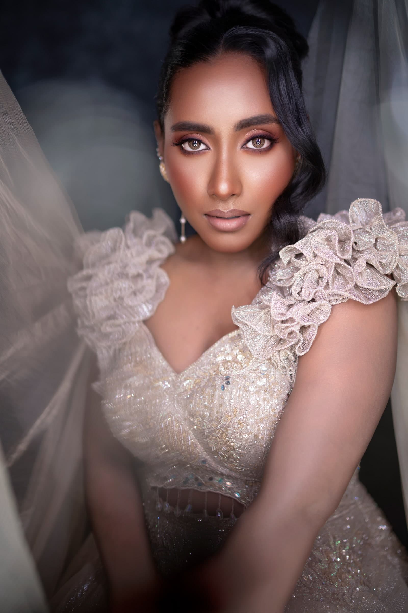 High-fashion editorial portrait framed in sheer tulle with luminous skin and defined eyes