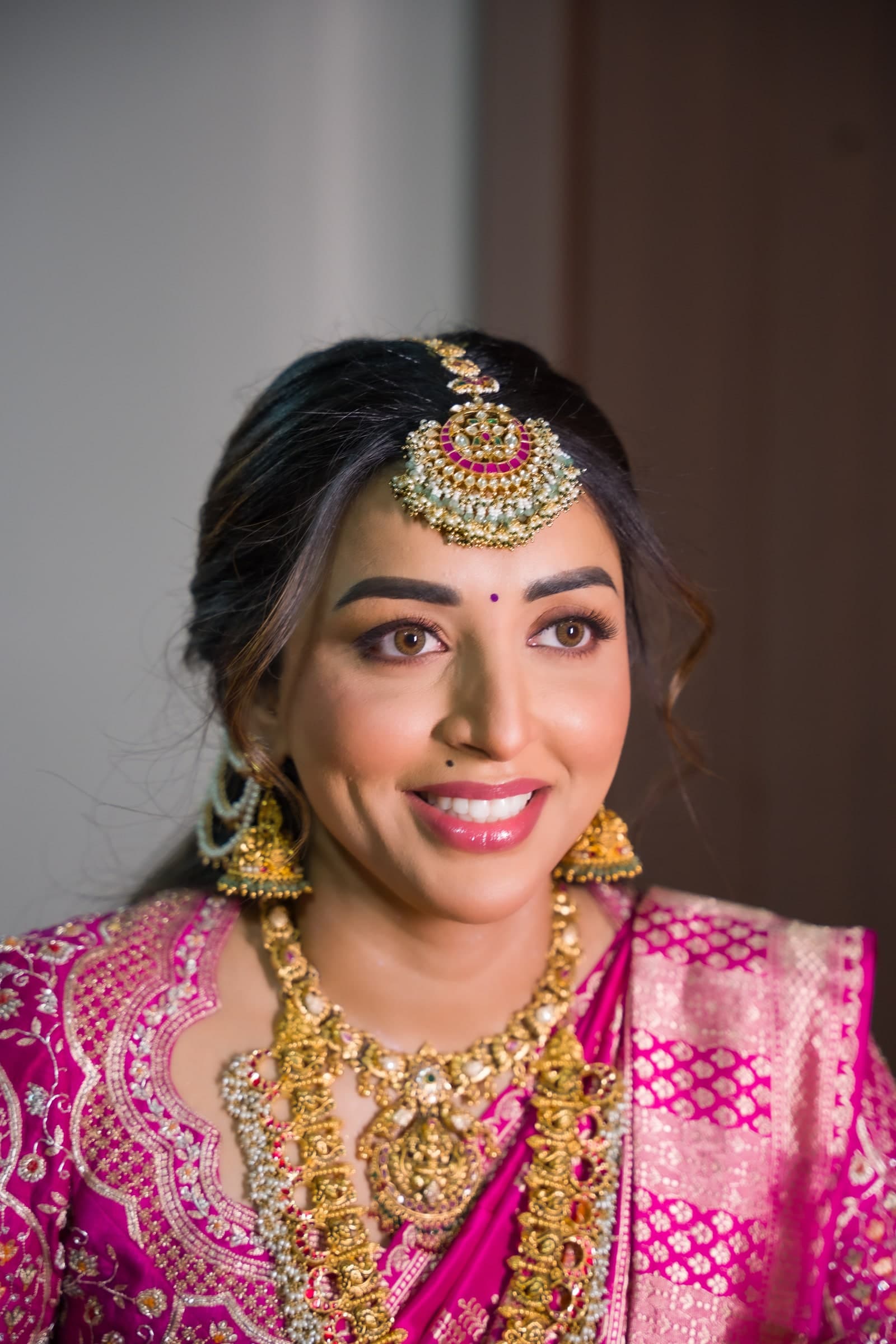Radiant bride in a magenta silk saree with traditional gold temple jewellery and a maang tikka