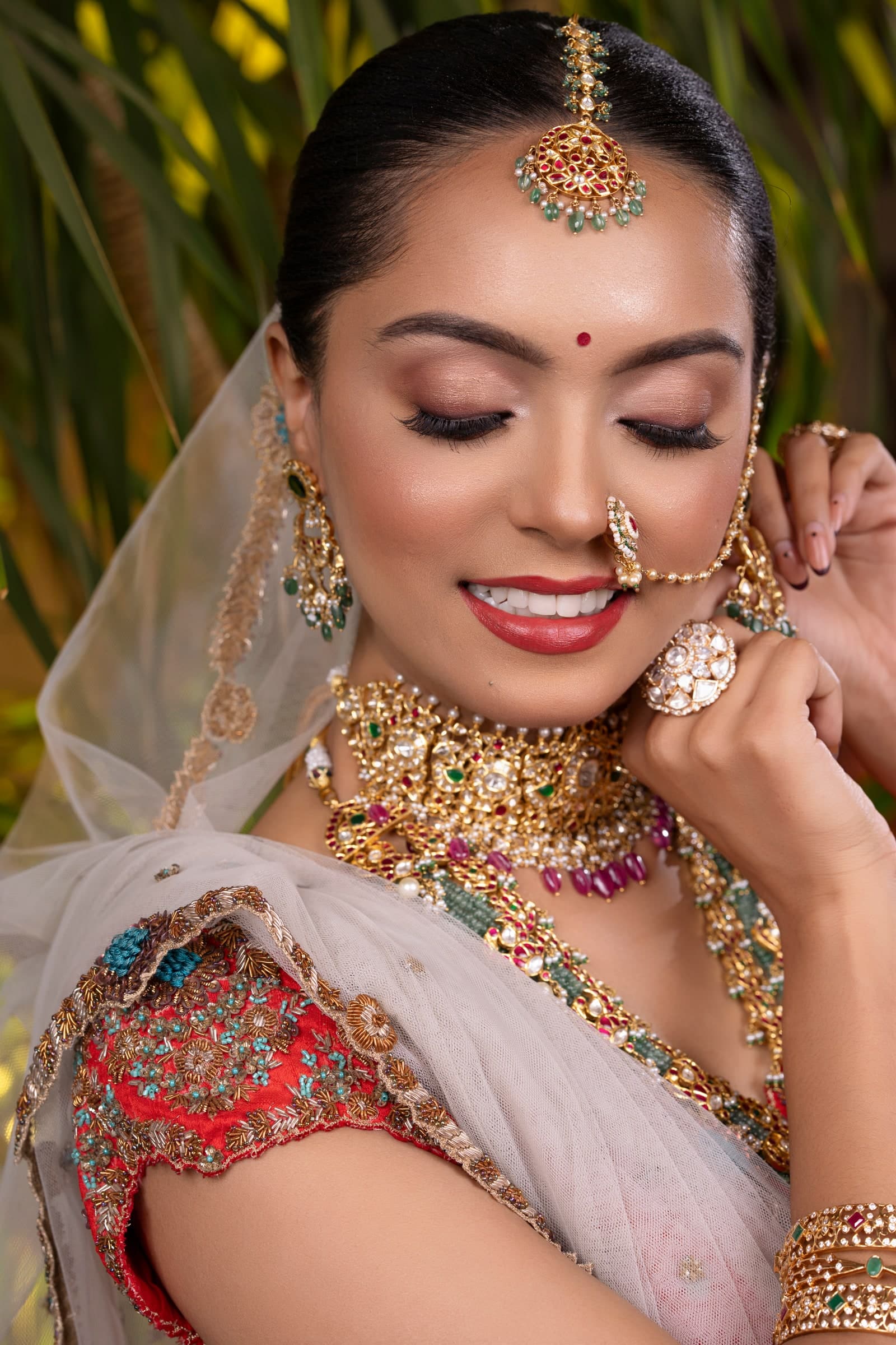 Bride in a red embroidered lehenga with a heavy kundan and ruby choker, nath and delicate veil