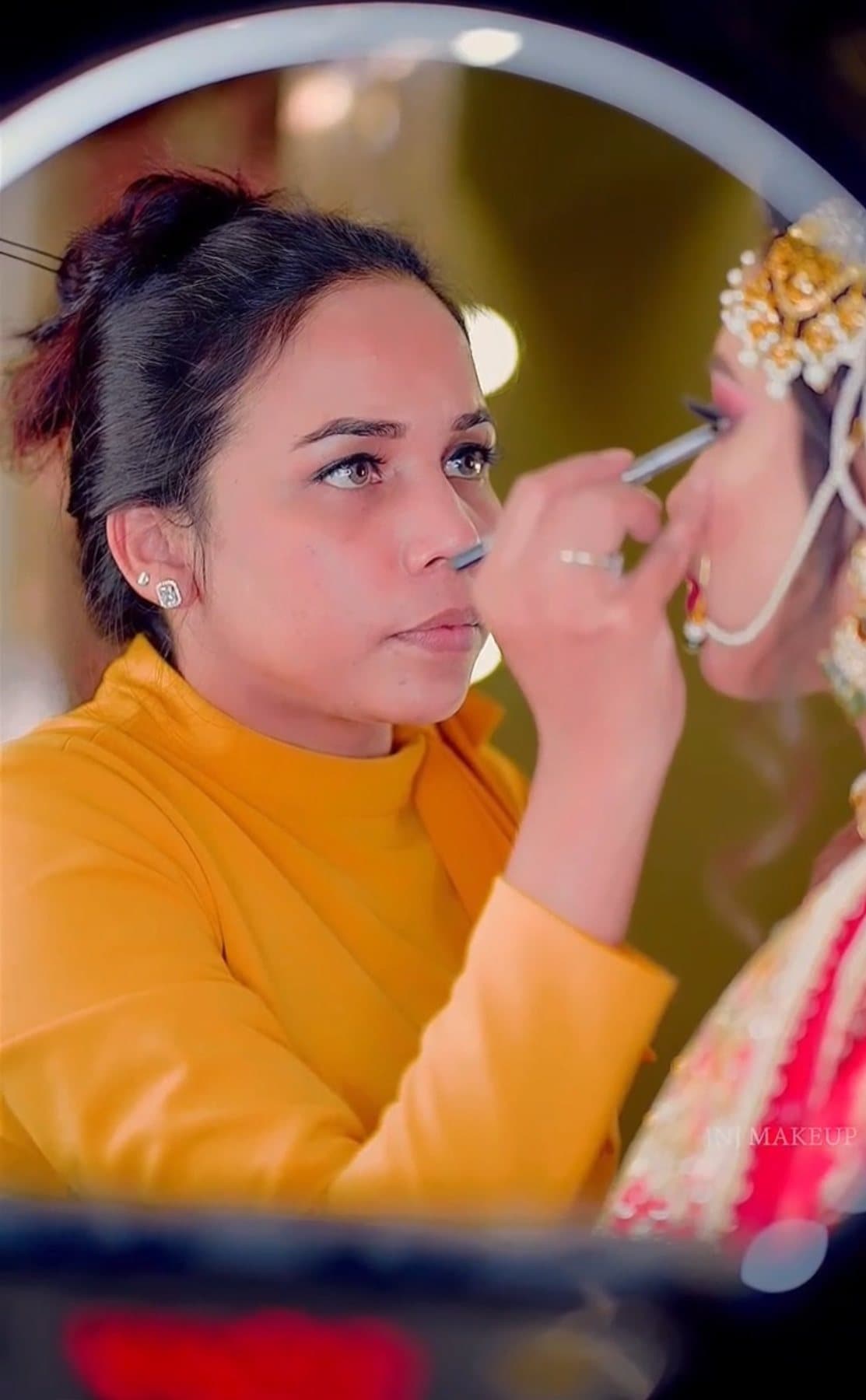 INJ makeup artist applying eye makeup to a bride, reflected in a ring-light mirror