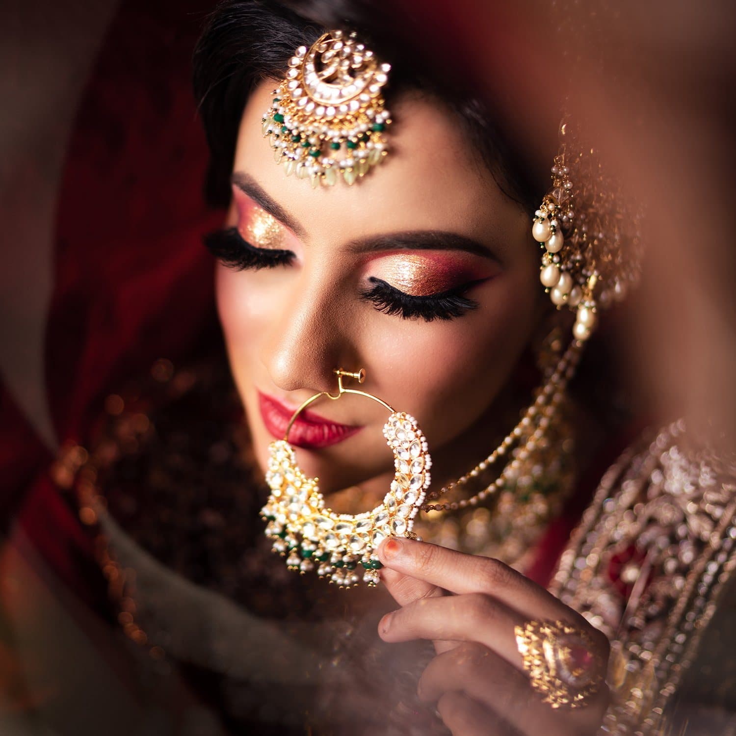 Bridal close-up with downcast eyes, a large gold nath and a soft rose lip