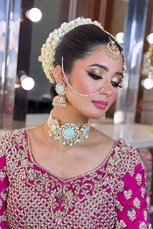 Bride in a magenta lehenga with a jasmine-adorned bun and turquoise jewellery