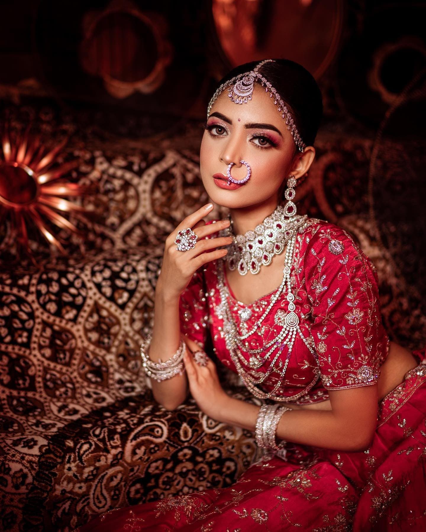 Bride in a red embroidered lehenga with diamond jewellery and a nath, styled by INJ Makeup Studio