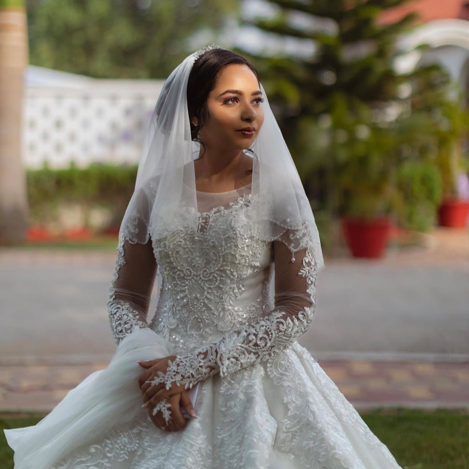 Bride in a white embellished gown and long veil in a garden setting